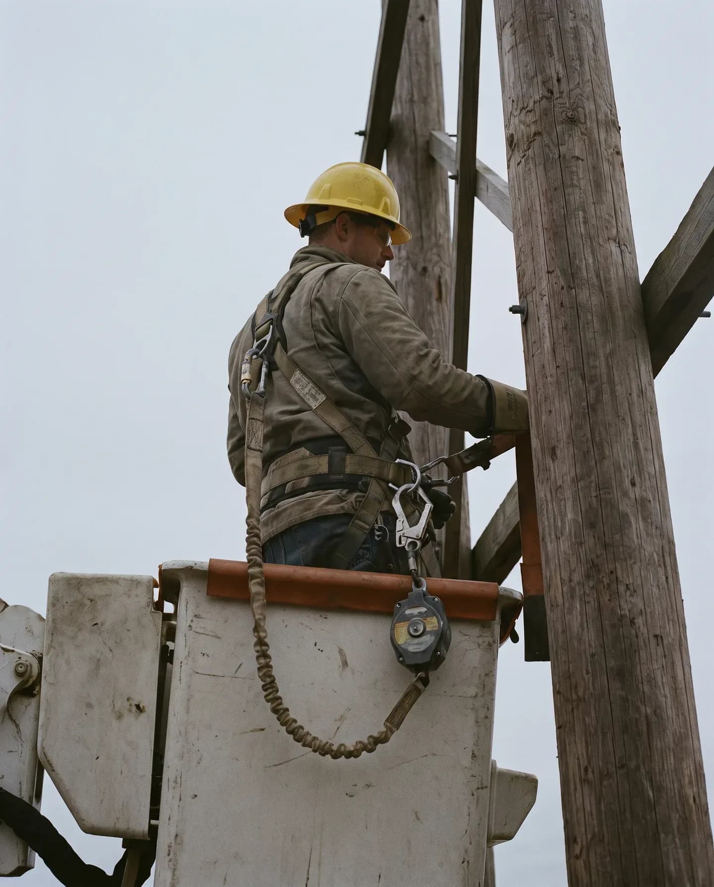 Lineworker in a harness working from an EWP bucket beside power poles